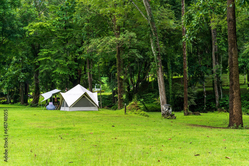 nature landscape camping or white glamping cabin tent on green grass lawn campground and tree with camper family holiday vacation on rainy season at khao laem national park in ka teng cheng waterfall