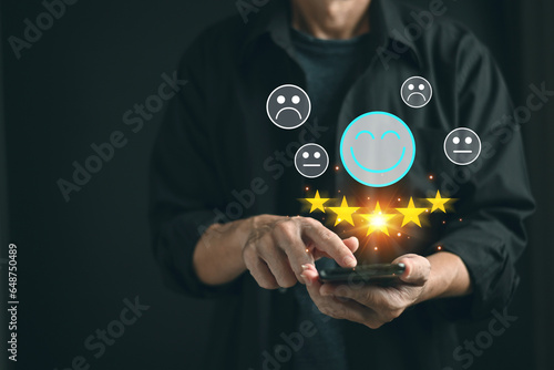Man hand press the smile face emoticon on smart phone screen and give five star symbol to increase rating of products and services concept, satisfaction survey,selective focus.