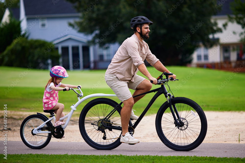 Obraz premium father and daughter, young kid cycling together. bicycle ride with towable bike trailer. active lifestyle for family with kids