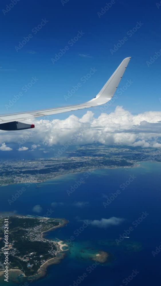 Aerial view of beautiful blue sea and tropical city through a window of an airplane, Travel or sightseeing, Vertical video for smartphone footage, Okinawa in Japan Aerial view of beautiful blue sea and tropical city through a window of an airplane, Travel or sightseeing, Vertical video for smartphone footage, Okinawa in Japan