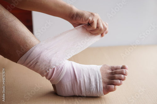 Hand is wrapping bandage around sprain ankle.  Concept, Health care and health problem, accident, first aid. Insurance.  Injury symptom treatment.            © Sanhanat
