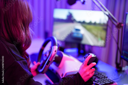 Asian young teenager driver girl playing super speed car game with steering wheel and gear controller simulation gadget closeup hand and monitor screen in entertainment neon gamer room photo