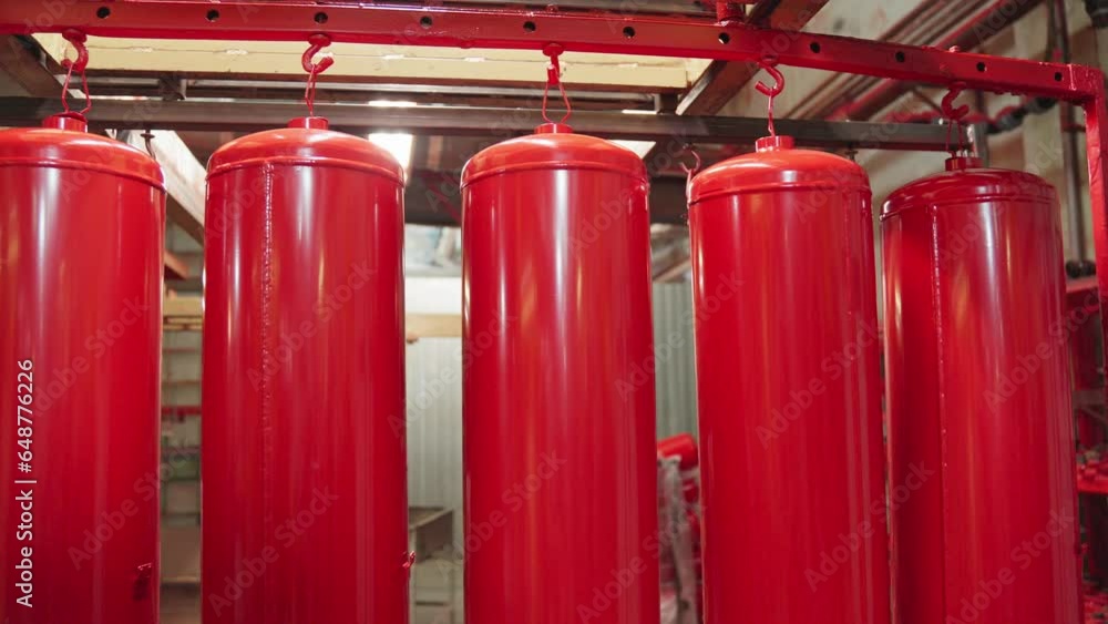 Worker spraying red paint on detail in painting chamber. Worker paints fire extinguishers with