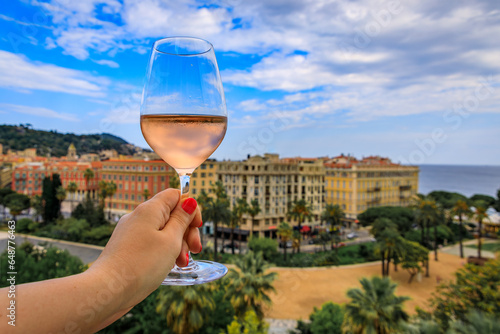 Woman s hand holding a glass of rose provencal wine at an outdoor restaurant with a background of blurred buildings in Old Town Nice, South of France
