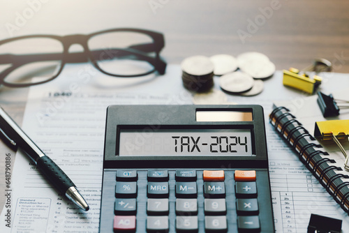 Word Tax 2024 on the calculator. Business and tax concept.Calculator, coins, book, tax form, and pen on table.Tax deduction planning.Financial research, government taxes, and calculation tax return photo