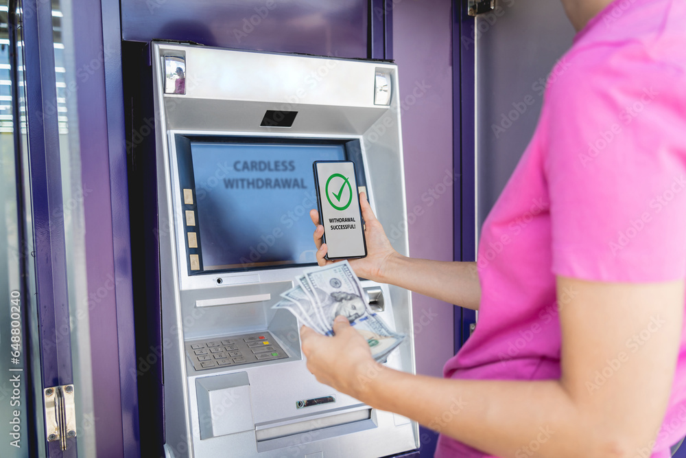 Young woman using the smart phone for cardless withdrawing the cash near the ATM Young woman using the smart phone for cardless withdrawing the cash near the ATM
