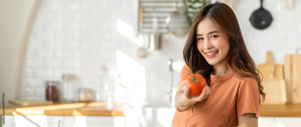 Portrait of beauty  healthy asian woman hold tomato, eating vegan food healthy with fresh vegetable in kitchen at home.diet, vegetarian, fruit, wellness, health, green food.Fitness and healthy food