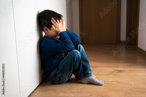 Upset problem child with head in hands sitting on floor concept for bullying, depression stress or frustration at home