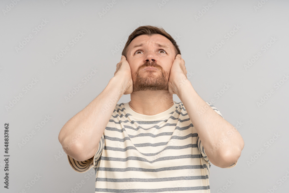 Man covers ears with hands looks up. Annoying noise loud sharp sounds. Sensory overload. Suffering from throbbing ear ache. Noisy neighbours stressed by hum avoid listening vociferous fight from above Man covers ears with hands looks up. Annoying noise loud sharp sounds. Sensory overload. Suffering from throbbing ear ache. Noisy neighbours stressed by hum avoid listening vociferous fight from above