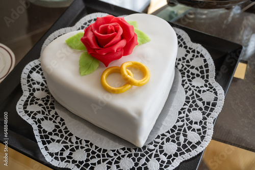 Herzförmige weiße Torte mit Marzipanrose und Eheringen