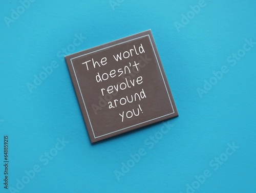 Brown card on blue background with handwritten text- The world doesn’t revolve around you - to remind we are the center of the universe, not as important that much, stop taking everything personally photo