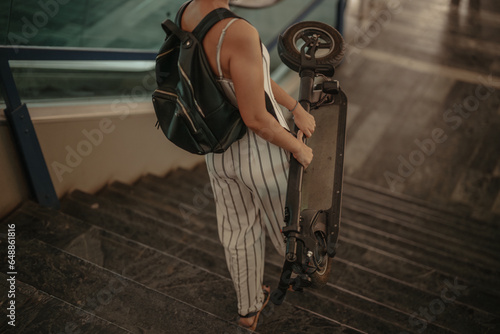 Businesswoman carrying electric scooter walking downstairs at business center. Going home after work.