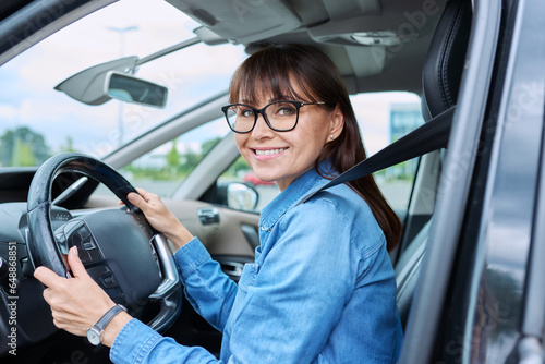 Middle-aged woman driver sitting behind wheel in car, smiling looking at camera © Valerii Honcharuk