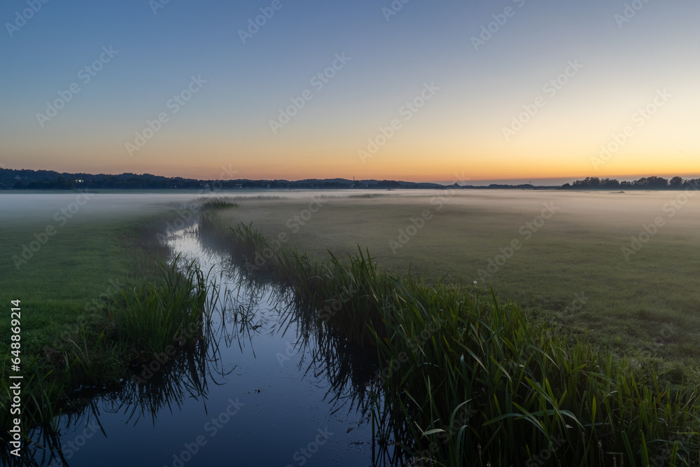 After a warm summer day, the sun slowly sets, and low-lying mist forms above the meadows along the coast of North Holland in the Netherlands.
