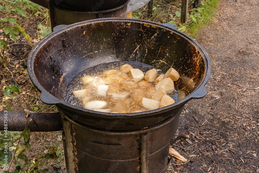 Coarsely chopped potatoes are fried in boiling oil in a cast-iron cauldron on a wood-burning stove. Street food Coarsely chopped potatoes are fried in boiling oil in a cast-iron cauldron on a wood-burning stove. Street food
