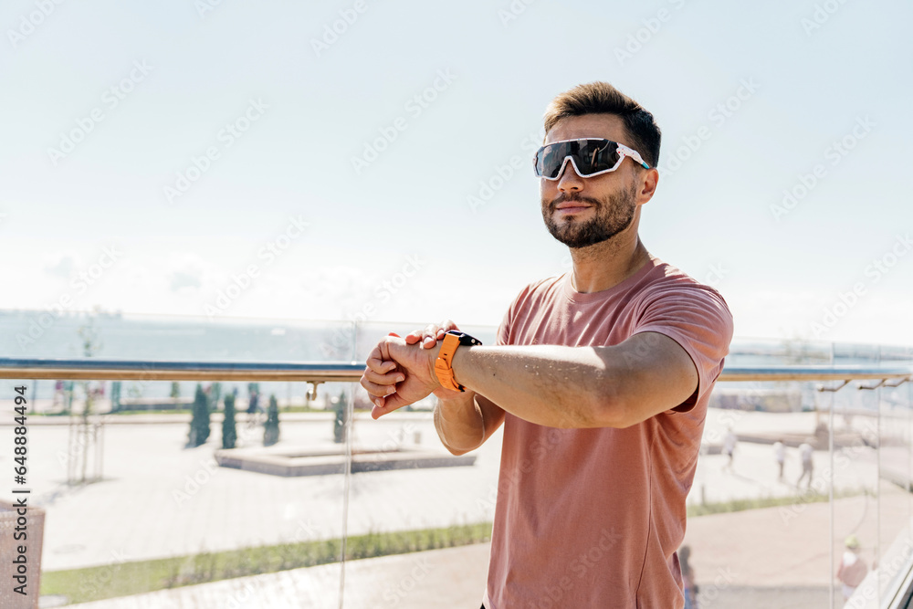 Uses a fitness watch man smiles exercise fitness for health.  Psychological therapy. The runner is a confident man, interval training. The athlete is happy in sportswear jogging.