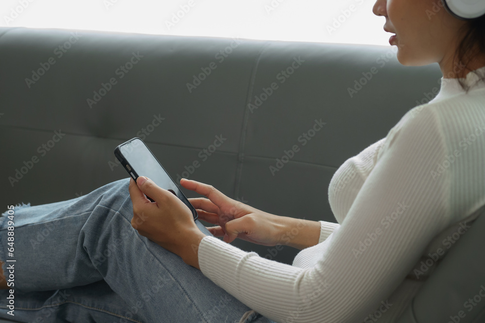Woman holding credit card using laptop and mobile phone to shop online on sofa in living room at home