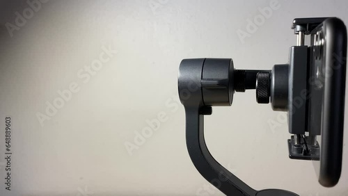 Black automatic gimbal stabilizer holding black phone on table against white wall indoor. with copy space. Technology and electronic gadget concept  photo