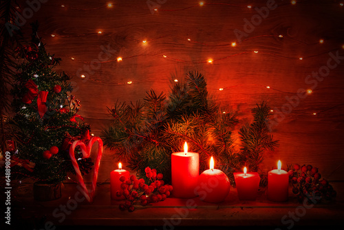 Christmas card with burning red candles, decorated with a Christmas tree, a heart made of striped candies and garland lights. Festive composition with red burning candles, a Christmas tree and a heart