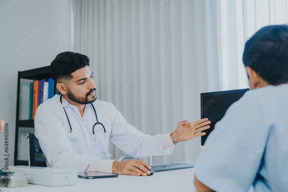 The Asian Muslim man doctor was sitting at the patient's examination table and was examining and talking about the patient with a smiling and worried face. The Asian Muslim man doctor was sitting at the patient's examination table and was examining and talking about the patient with a smiling and worried face.