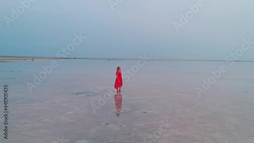 Aerial of a young woman in red dress standing in the water of a unique pink salt lake. Sunset at lake Bursol with beautiful reflections on calm water surface. Stunning scenery photo