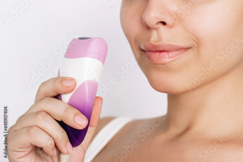 Schilderij op canvas Cropped shot of young caucasian woman holding epilator in her hand for getting rid of unwanted hair on a white background