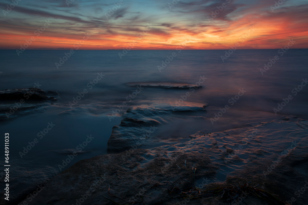Long exposure of sea waves over flat rocks at the sunset.