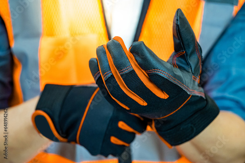 Photography Male construction worker with reflective orange vest putting black protective gloves on his hands