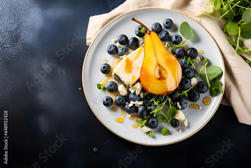 Baked Pear and blue cheese salad served on white plate with blueberries, mIcrogreens and honey topping on dark background with copy space. Pear salad commercial banner. Gourmet dish, healthy eating photo