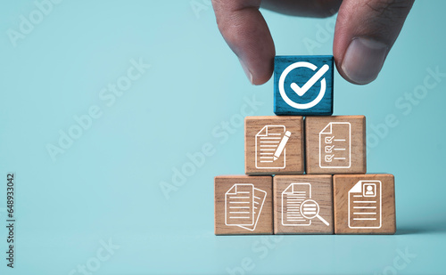 Hand holding white correct sign mark on blue wooden block cube and the top of document icon for ISO quality control certification and project approval concept. photo