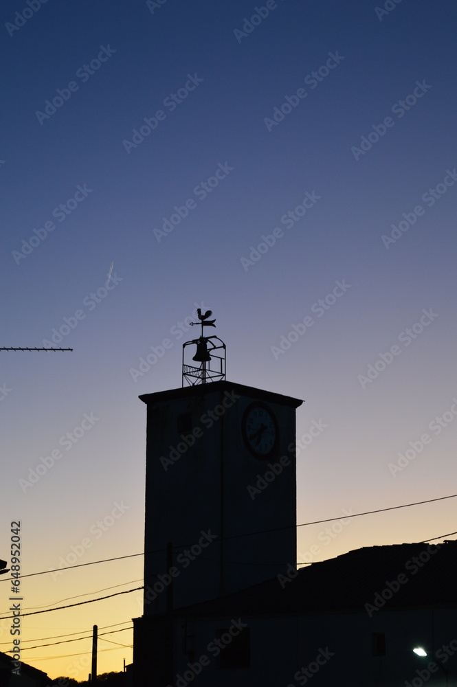 Fotografía de la torre de un campanario con una veleta con forma de gallo.