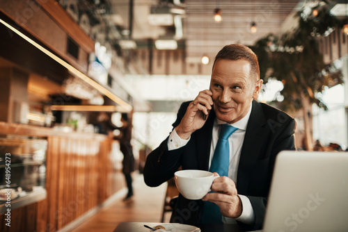 Middle aged businessman talking on a smartphone while having coffee in a cafe decorated for christmas and the new year holidays