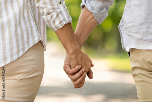 Unrecognizable mature man and woman holding hands while walking together in park