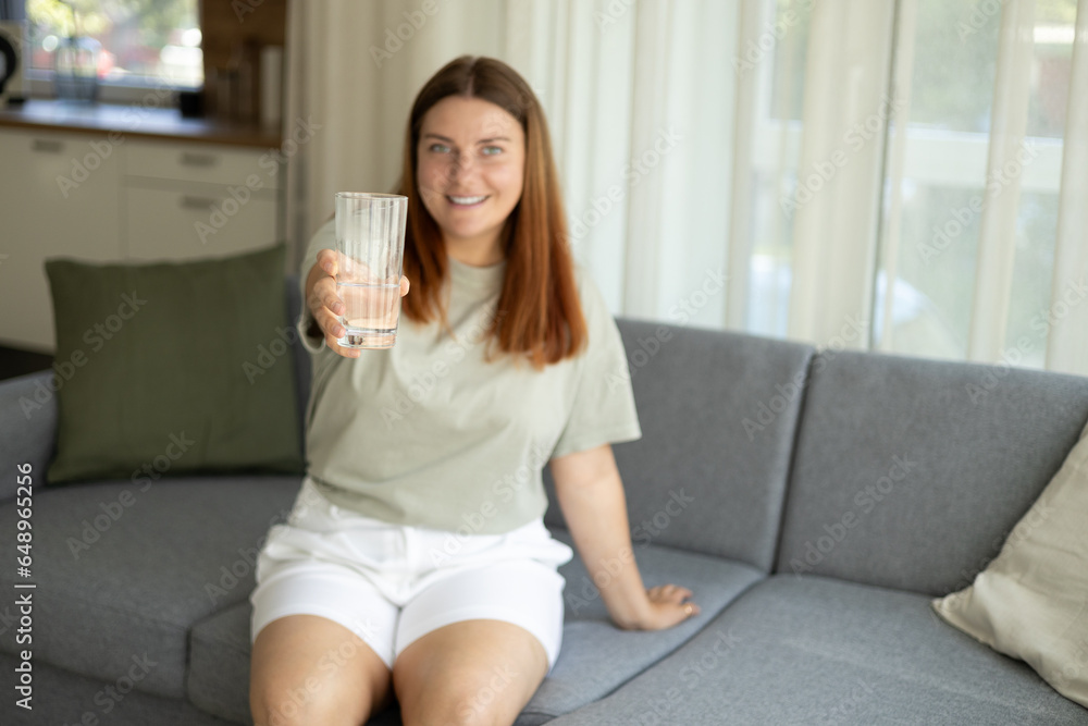 Young woman drinking pure water from glass and sitting on textile couch at home. Health care concept photo, lifestyle, close up Young woman drinking pure water from glass and sitting on textile couch at home. Health care concept photo, lifestyle, close up