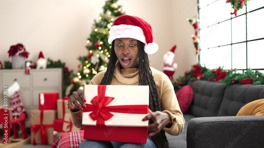 African woman unpacking gift sitting by christmas tree at home African woman unpacking gift sitting by christmas tree at home