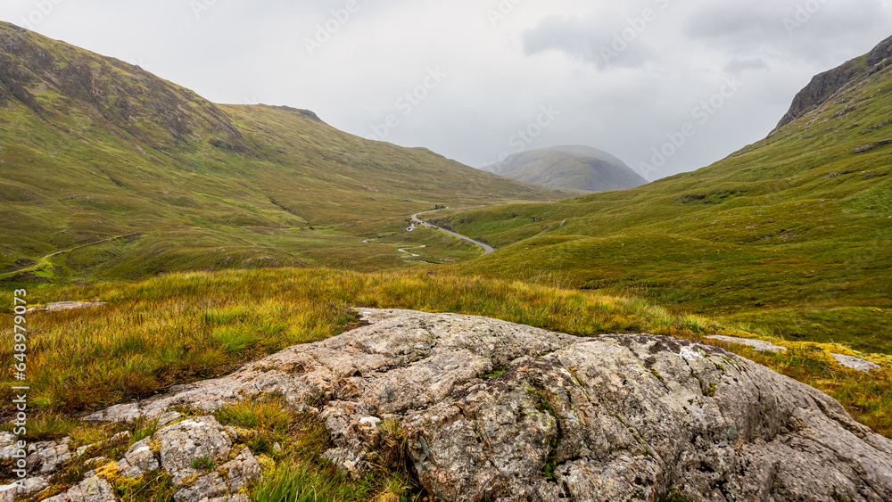 Fog-covered green mountains and hiking trails in the Glencoe Valley, Scotland.