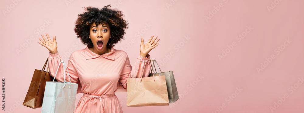 Fototapeta premium An african american woman dropping shopping bags, surprised face with mouth open, pastel pink background copyspace, low prices sale and discounts for black friday concept