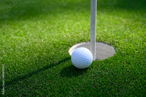 Closeup of white golf ball next to the cup on a putting green 