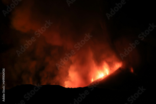 Etna panoramica di notte sul vulcano in eruzione con lava tra cenere gas e vapore nel cielo notturno dal cratere del 13 Agosto 2023 