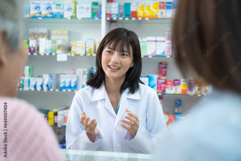 Young Asian pharmacist talking with customer at pharmacy counter. She tells customers about drug information at the pharmacy.