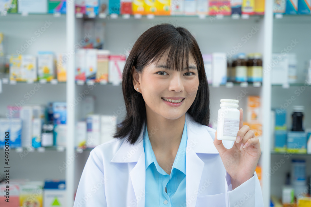 Young asian female pharmacist holding drug to camera with smiling at pharmacy counter. She holding drug with smiling at pharmacy shop.
