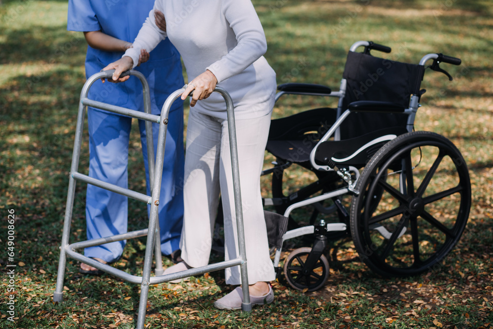 Fototapeta premium Asian young woman nurse at nursing home take care disabled senior man. Caregiver doctor serve physical therapy for older elderly patient to exercise and practice walking on walker or cane at backyard.