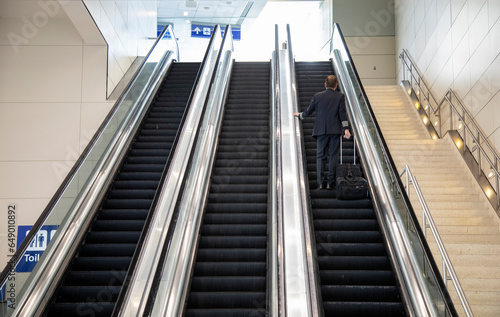 Airline captain with suitcase riding an escalator at an airport