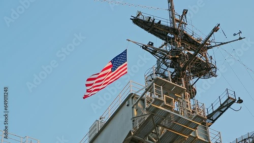 American flag flies on the mast of a warship. View of us flag on navy ship. USA flag and antennas on carrier control tower in blue sky. United States warship flying the American flag