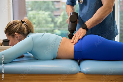 Male therapist massaging female spine and lower back with massage gun