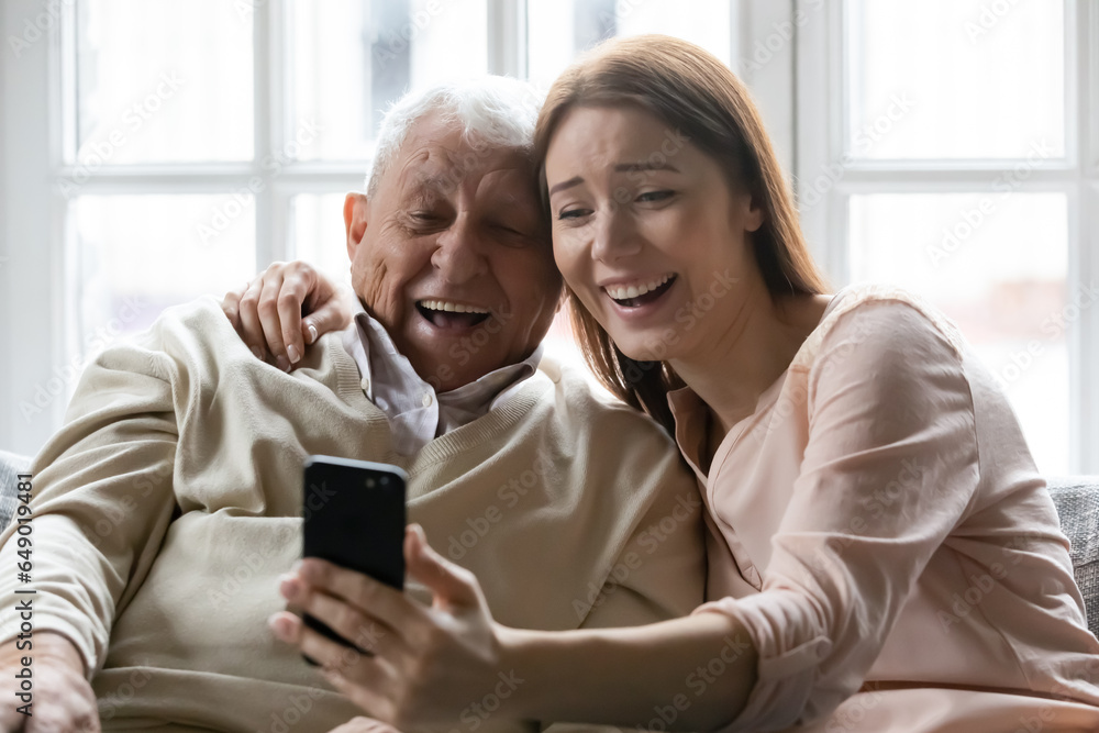 Overjoyed old 80s father and adult daughter relax at home have fun making self-portrait picture on cell, happy elderly dad and grownup child smile laugh take selfie on smartphone at home together Overjoyed old 80s father and adult daughter relax at home have fun making self-portrait picture on cell, happy elderly dad and grownup child smile laugh take selfie on smartphone at home together