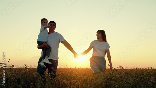 Mom dad child walk hand in hand. Happy family of farmers with child, are walking on wheat field. Slow motion. Mother father, little daughter enjoying nature together outdoor. People travel. Silhouette