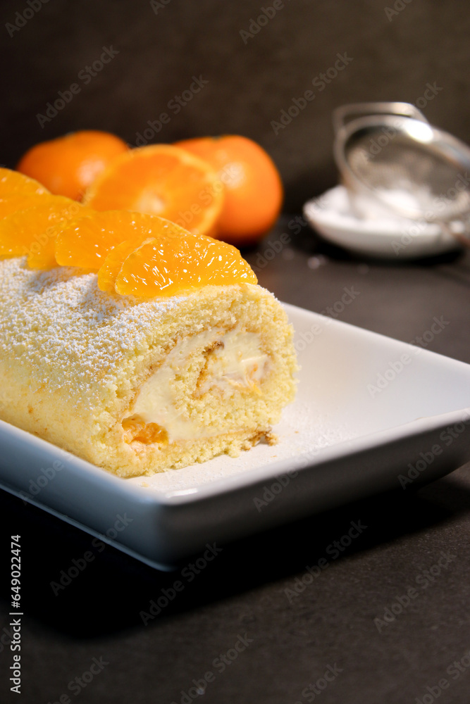 Delicious homemade mandarin cake roll with buttercream feeling, white plate and grey table background 