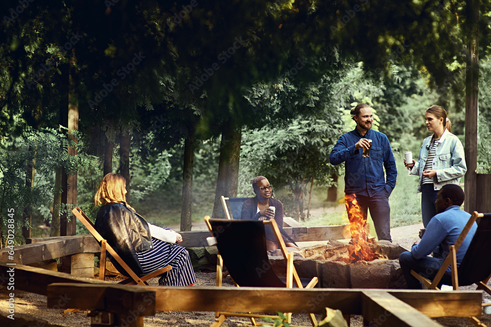 Multicultural group of friends enjoying beer by the campfire on a summer evening. Camping, tourism, holiday, outdoors concept. Barbeque party. Corporate team building event. Active lifestyle. - obrazy, fototapety, plakaty 