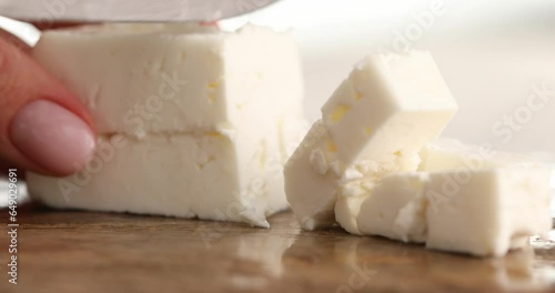 Close-up of Cutting or slicing cubes of feta cheese on a board for a Greek Salad. Healthy food.